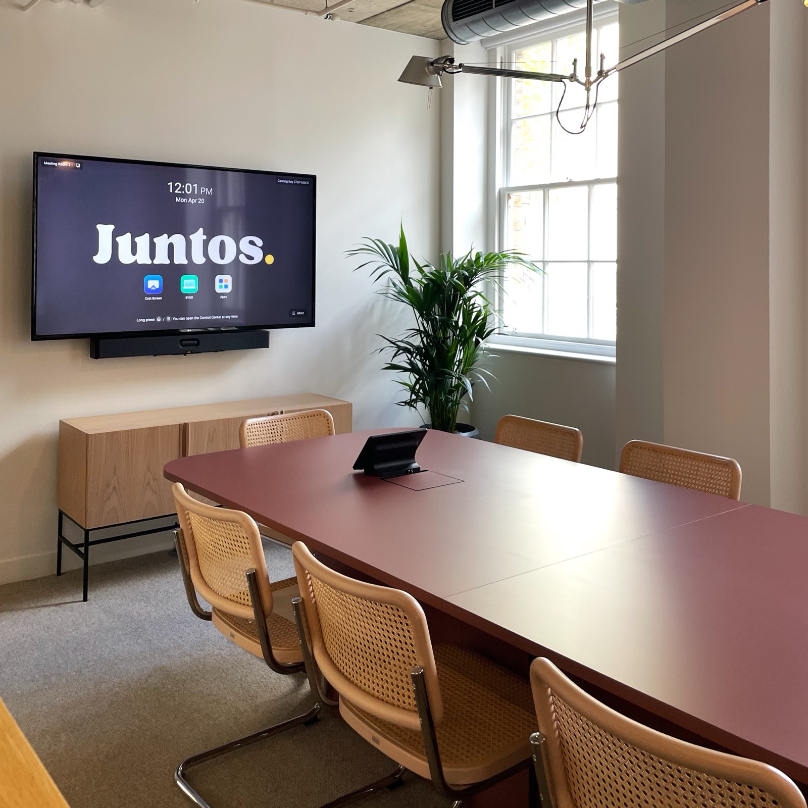 A Juntos meeting room — burgundy table, cane Cesca chairs and a Juntos-branded display